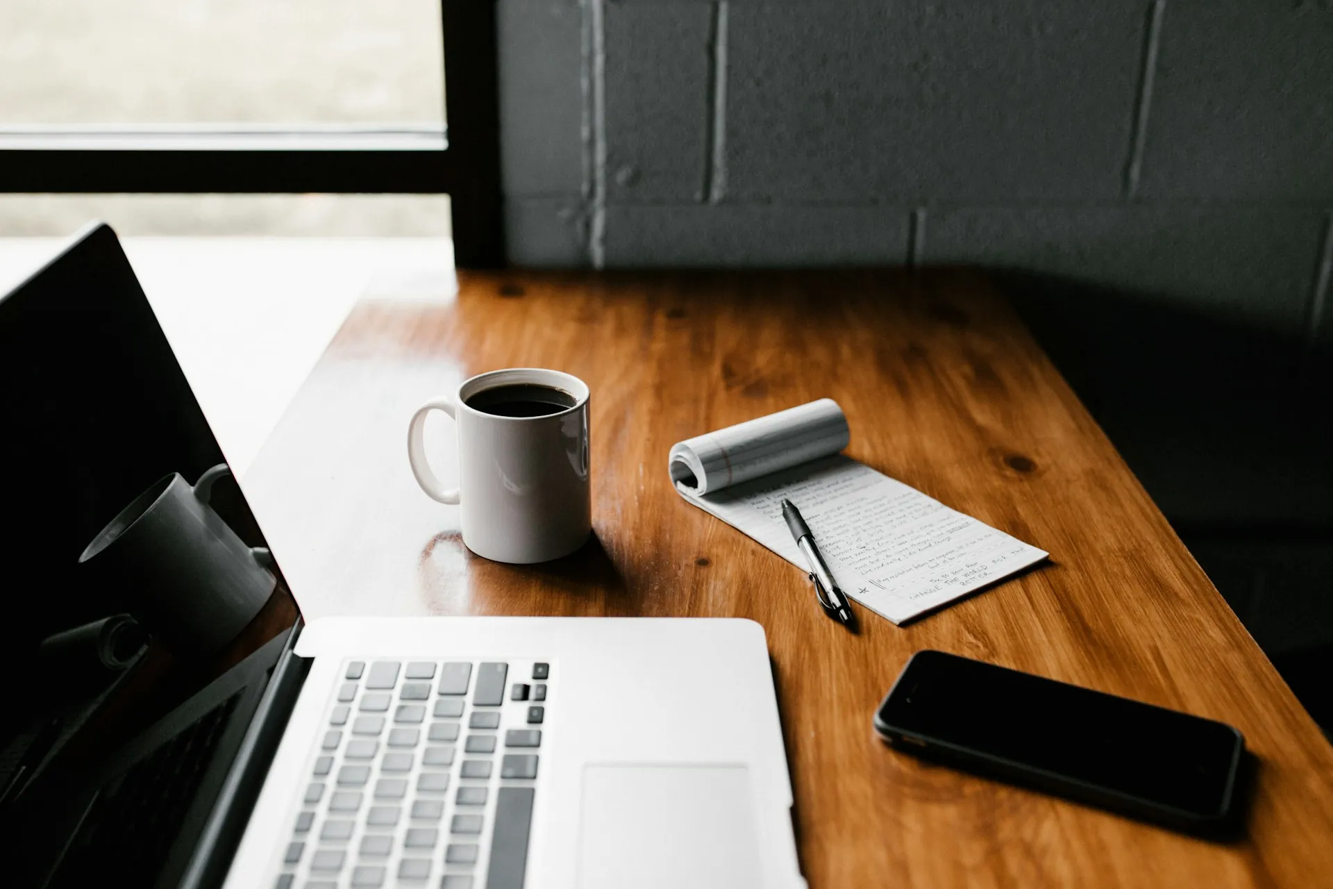 A laptop on a desk by a large window